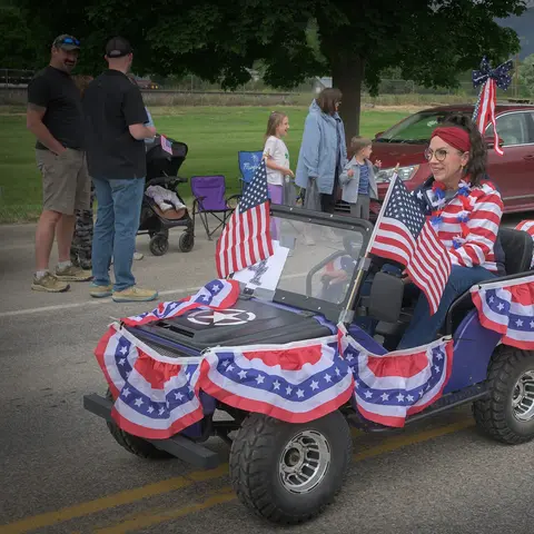 A woman sits in a small decorated vehicle with American flags during an outdoor event.