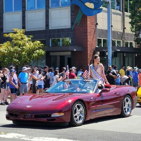A woman in a sash rides in a convertible car in a parade.