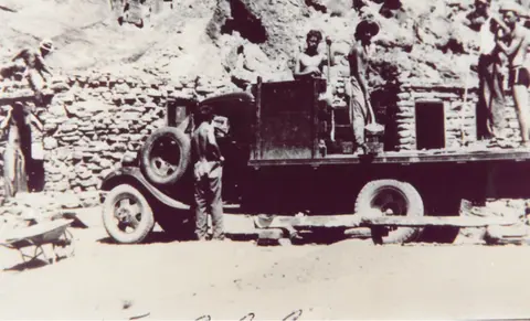 Historic black and white photograph showing workers around a truck at a stone construction site.