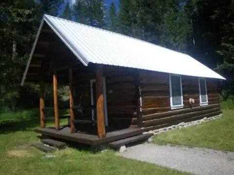 A log cabin with a white metal roof stands surrounded by trees.
