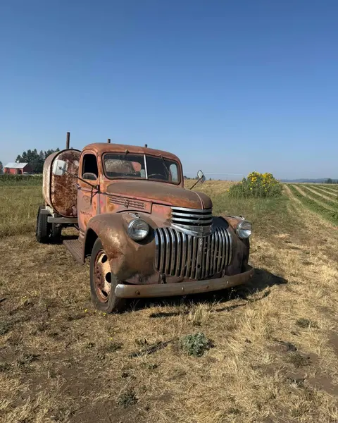 An old, rusty truck with a tank on the back parked in a field.
