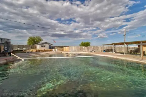An outdoor swimming pool with clear water and a volleyball net under a partly cloudy sky.