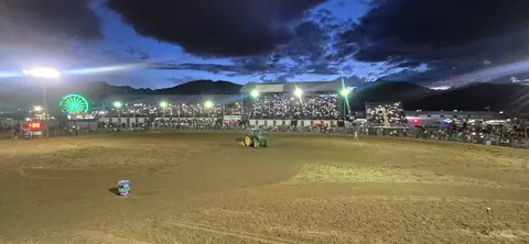 A dirt arena at night with a large crowd in grandstands under a dark sky.