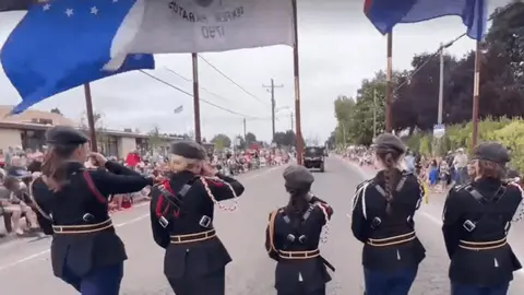 A group of people in uniform march in a parade carrying flags down a street.
