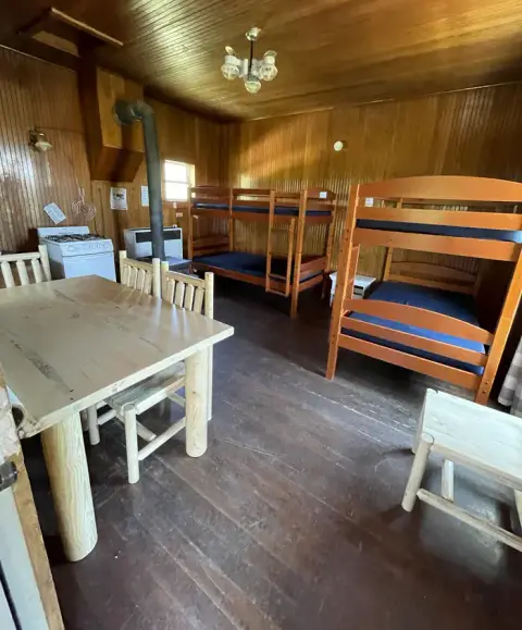 An interior shot of a rustic cabin featuring wooden bunk beds, a dining table, and a stove.