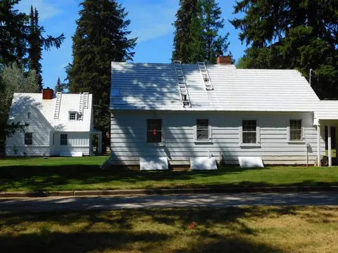 Exterior view of two white houses surrounded by tall trees and green grass.