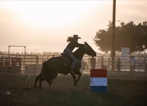 A person rides a horse in a rodeo arena.