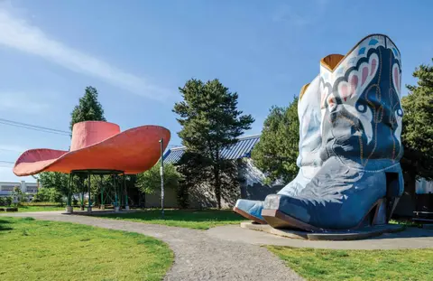 Giant cowboy hat and boot sculptures stand in a park.