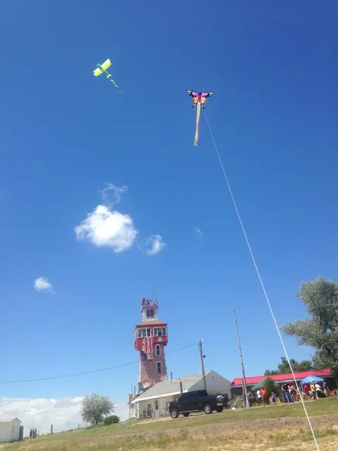 Two kites fly in a bright blue sky above a red-and-white tower.