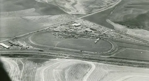 An aerial view of a racetrack with a large parking lot and surrounding fields.