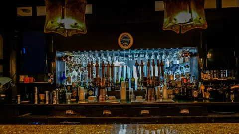 An interior view of a dark wooden bar with beer taps and glassware hanging above.