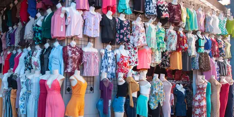 A display of many colorful women's clothes on mannequins and hangers against a wall.