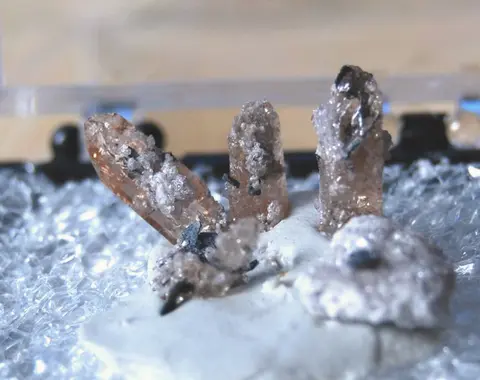 A close-up photograph of mineral crystals displayed inside a small box.