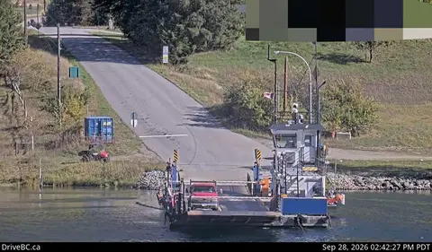 A ferry carrying a vehicle approaches a ramp by the water.