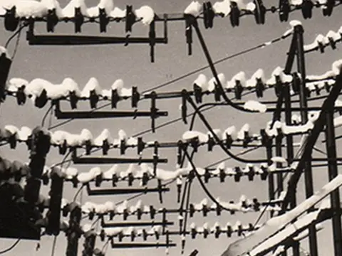 A historic photograph shows snowy utility poles with tangled wires and insulators.