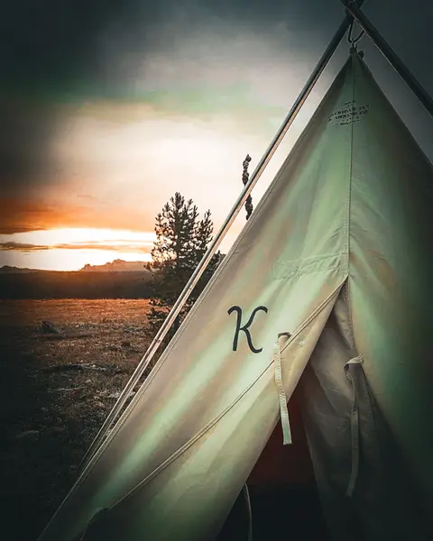 A tent stands in an open landscape at sunset.