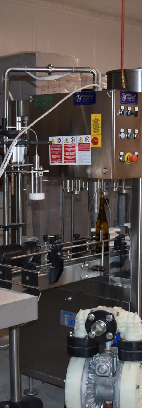 A bottling machine in a winery with a wine bottle on the conveyor belt.