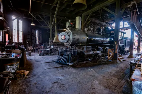 A vintage steam locomotive parked inside a rustic workshop.