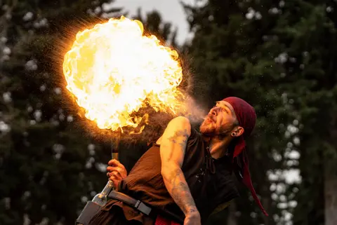 A performer breathes a large fireball outdoors.