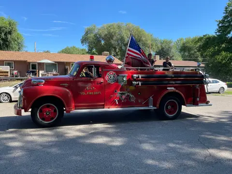 A vintage red fire truck is parked on a street with an American flag displayed on the back.