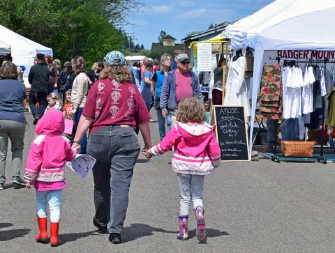 People walking through an outdoor market with vendor booths.