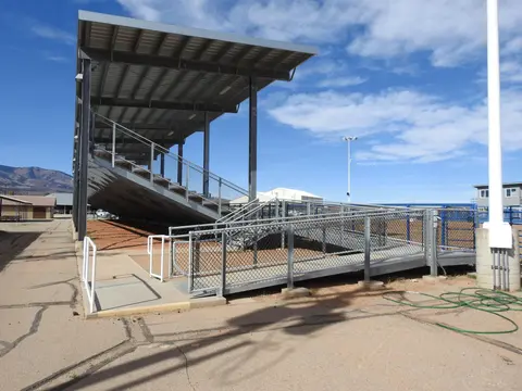 An outdoor set of covered stadium bleachers with a ramp under a blue sky.