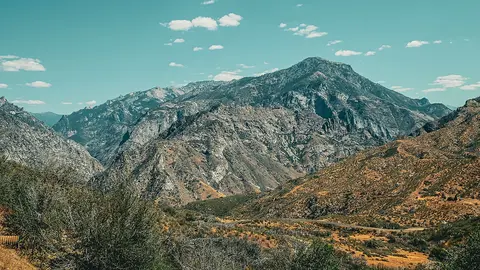 A landscape photograph showing rugged mountains under a blue sky with scattered clouds.