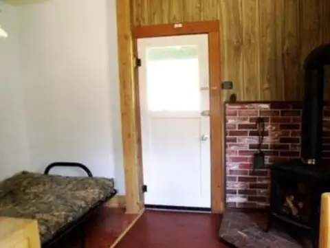 An interior view of a room with a bed, door, and wood stove.