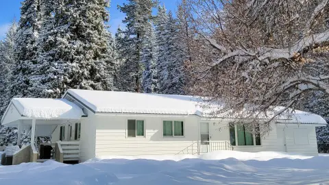 A white house surrounded by snow and tall pine trees.