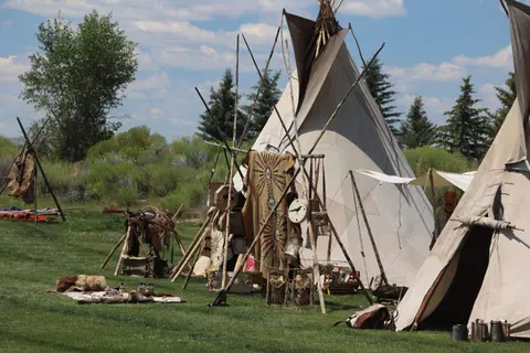 A campsite with tipis, hides, and other historical artifacts outdoors.