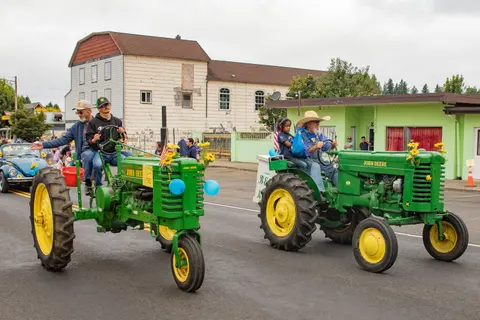 People drive two vintage green tractors in a parade.