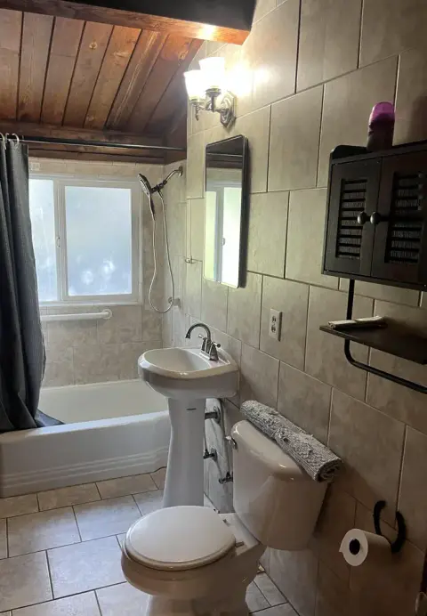 A tiled bathroom features a pedestal sink, toilet, and bathtub with a shower.