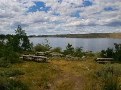 Picnic tables near a scenic lake under a cloudy sky.