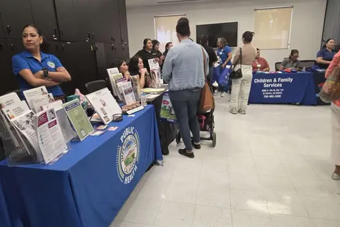 People gather around informational tables inside a community room.