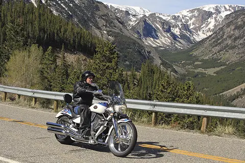A person rides a motorcycle on a winding road through a mountain range.