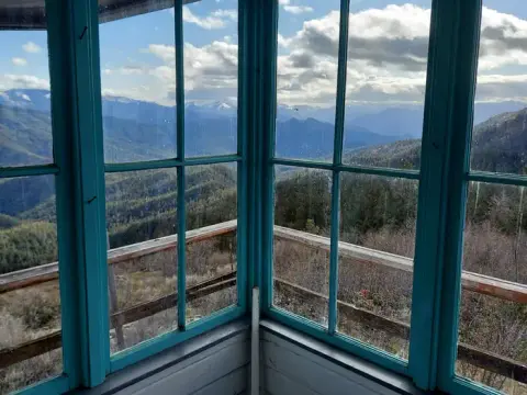 A view of mountains and forests from inside a fire lookout tower.