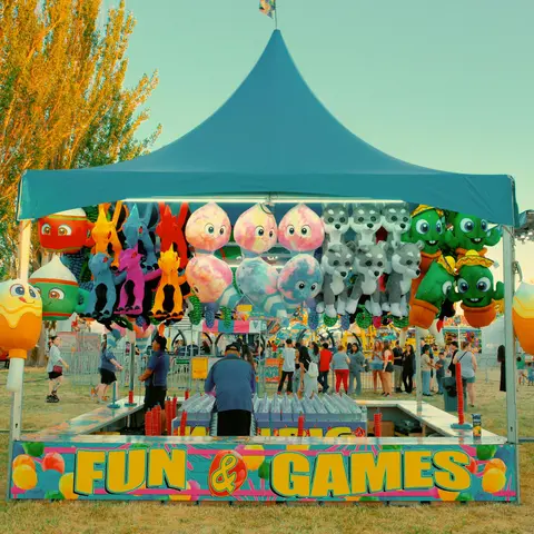 A carnival game booth with colorful stuffed prizes hanging under a blue canopy.