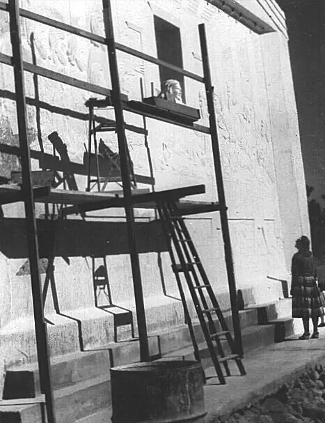 A historic black-and-white photograph shows scaffolding and a person working on an exterior wall.