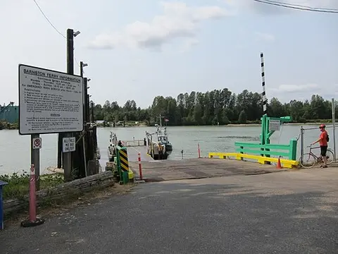 A ferry docked at a river terminal with an information sign and a person standing with a bicycle.
