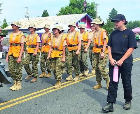 A group of people in uniform and orange vests walking on a street.