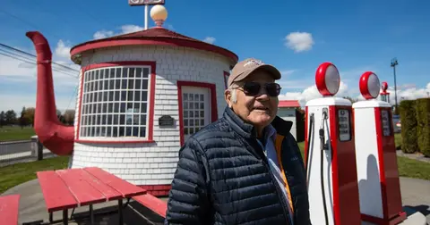 A man stands in front of a teapot-shaped building and old gas pumps.