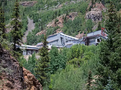 An industrial structure is nestled in a lush mountainous landscape.