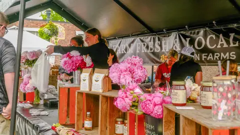 People at a farm fresh market stand with flowers and jars.