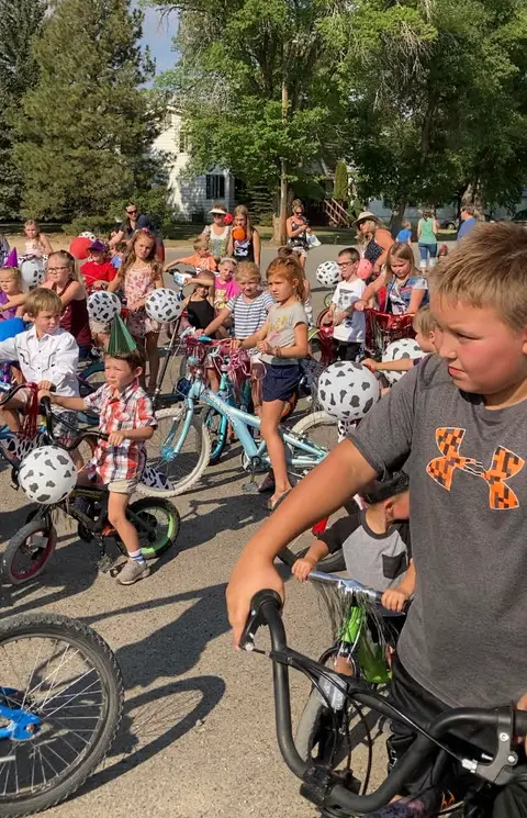 A group of children and adults gather outdoors with decorated bicycles.