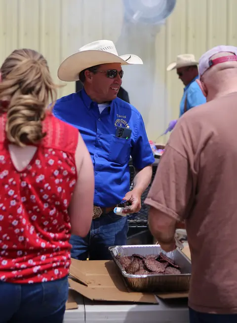 A man wearing a cowboy hat and blue shirt serves food from a pan outside.