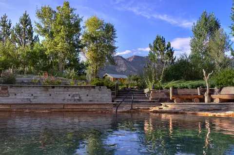 An outdoor pool surrounded by lush greenery and mountains under a blue sky.