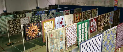 Many colorful quilts are displayed on racks in a large indoor space.