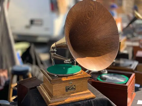 An antique gramophone with a wooden horn is displayed outdoors.