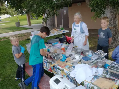 An instructor and children prepare food at a table outdoors.