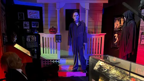 An indoor display featuring horror movie props and mannequins, including a Michael Myers figure standing on a porch set.